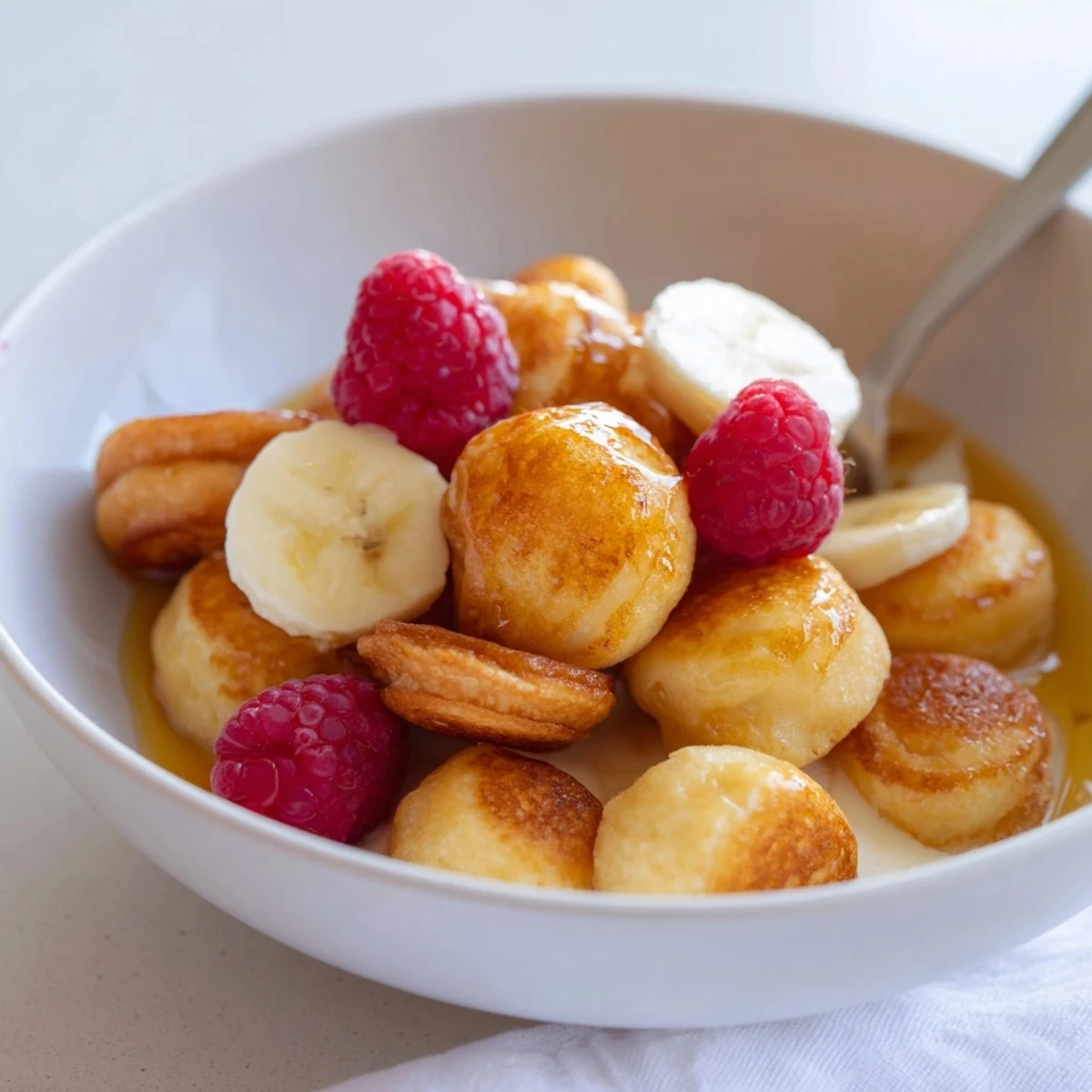 Delicious mini pancake cereal served in a bowl with maple syrup and fresh berries.  