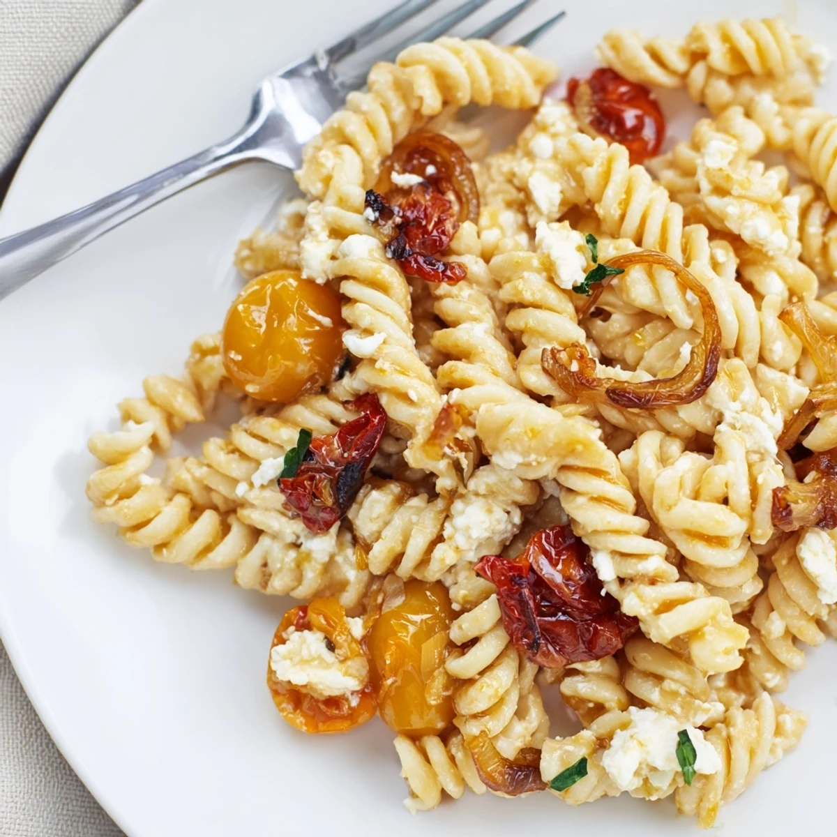 Golden feta melted among pasta, sun-dried tomatoes, and fresh basil garnish.