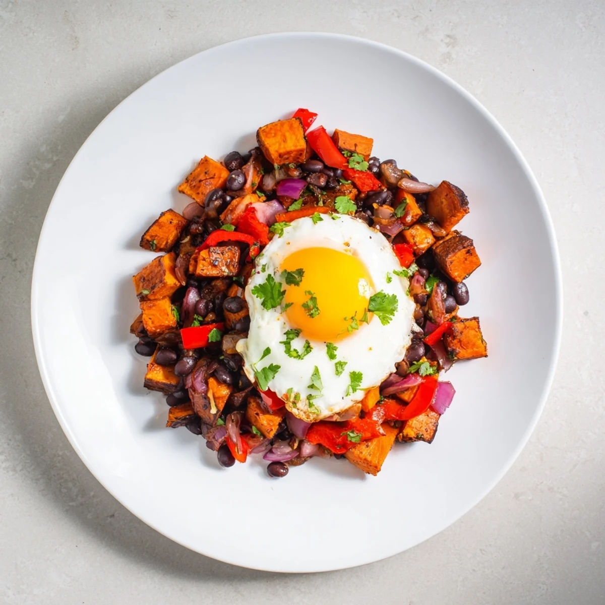 Steaming Sweet Potato & Black Bean Breakfast Hash topped with sunny-side-up eggs, a perfect morning meal.