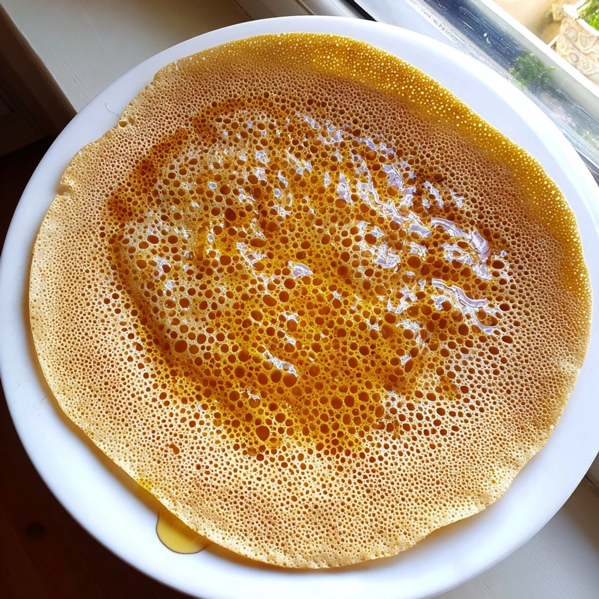 Golden, bubbly Moroccan Baghrir crepes are ready, drizzled with honey, perfect for breakfast.