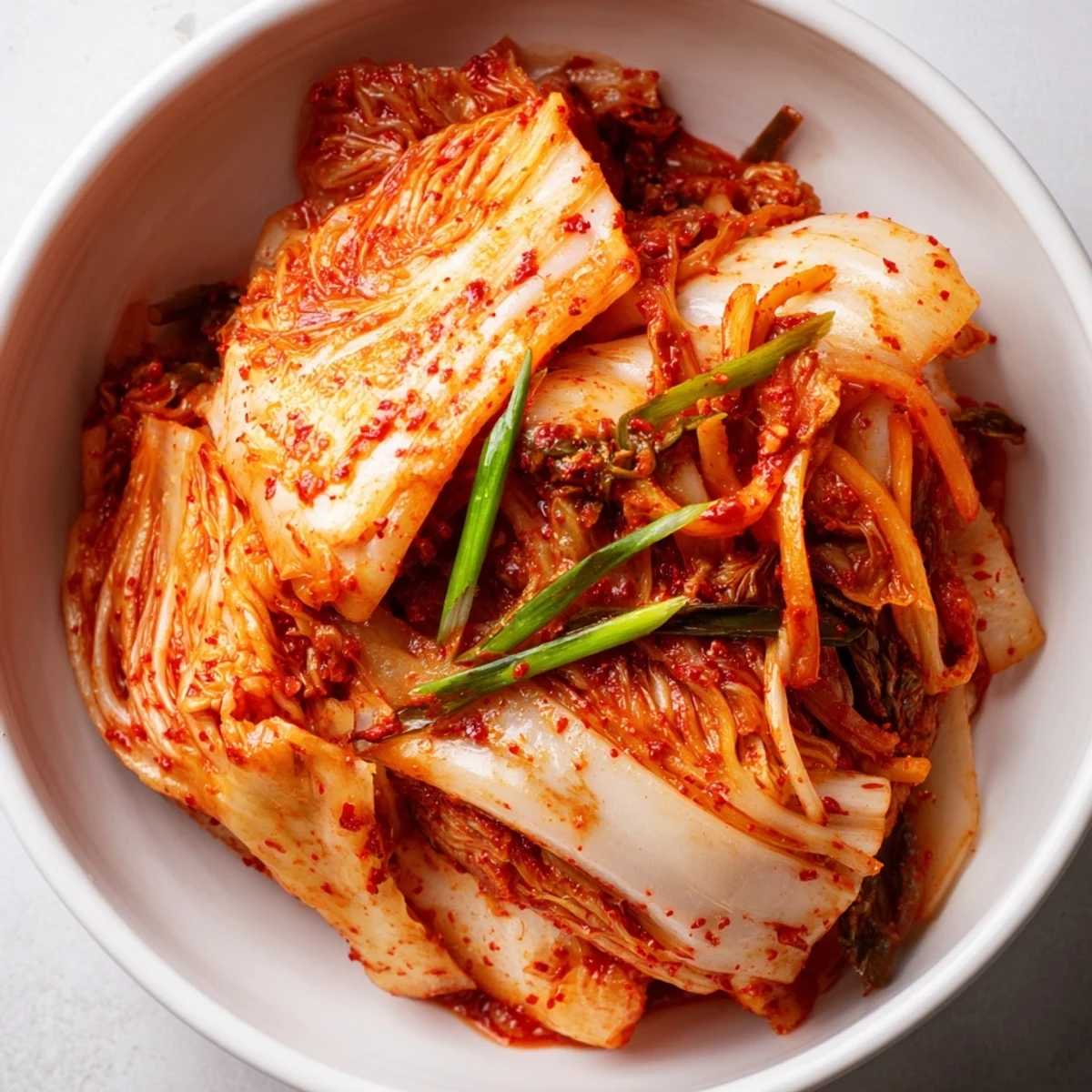 Close-up of freshly mixed kimchi in a glass jar, showcasing layers of red chili flakes and fresh vegetables before fermentation.