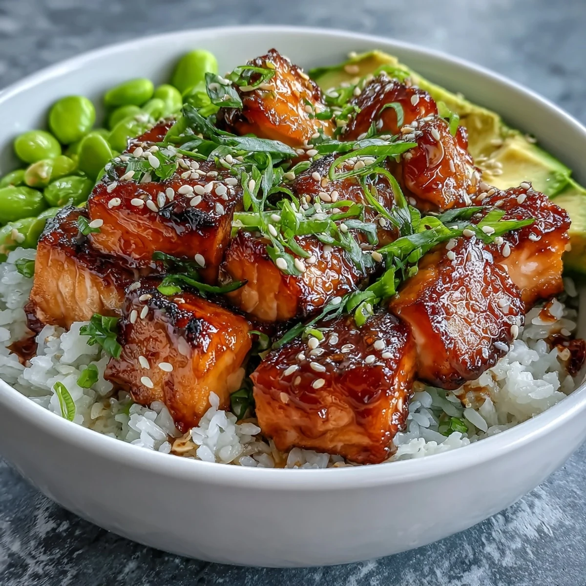 Flaky, glazed salmon cubes sit on fluffy jasmine rice with creamy avocado slices and bright green edamame.