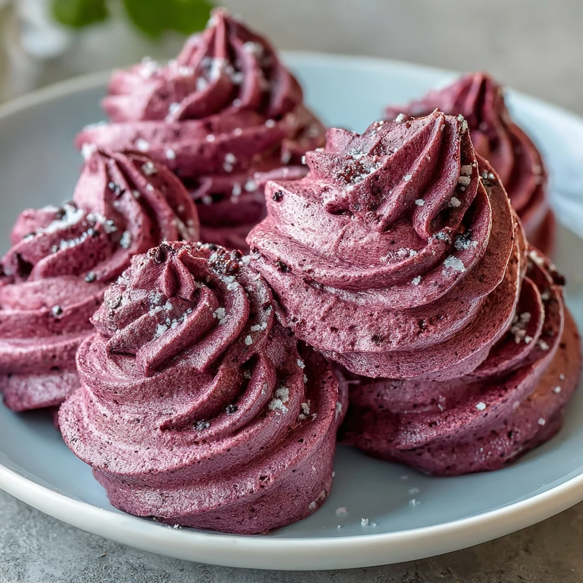 Freshly baked Black Currant Meringues, crisp and light, served on a white plate next to fresh berries.