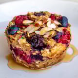A close-up of baked oatmeal cups showing plump berries and creamy almond butter swirling within.