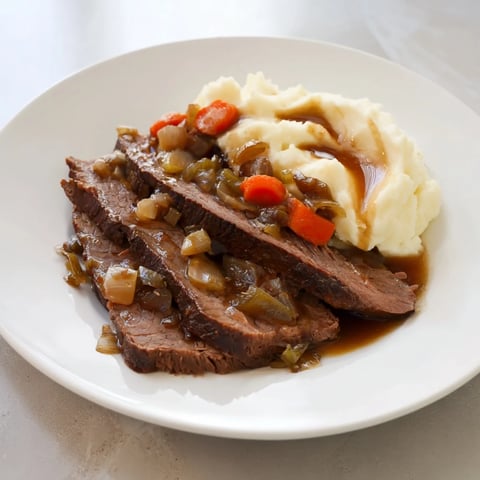Tender slices of classic brisket sit atop creamy, vibrant mashed sweet potatoes for a beautiful meal.