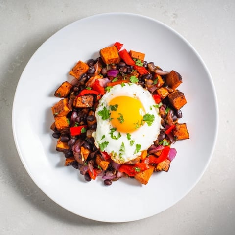 Steaming Sweet Potato & Black Bean Breakfast Hash topped with sunny-side-up eggs, a perfect morning meal.