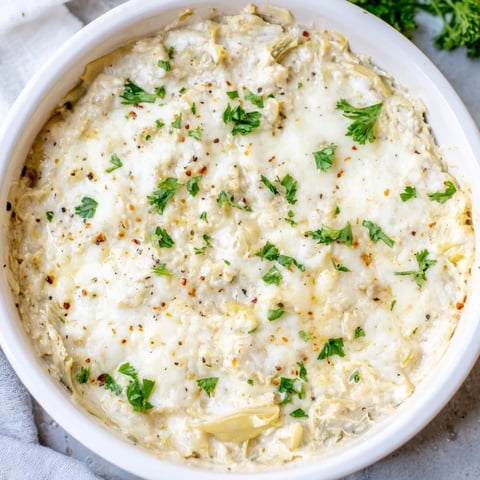 Golden brown Baked Artichoke Dip, bubbling and ready, served with crispy crackers for dipping.