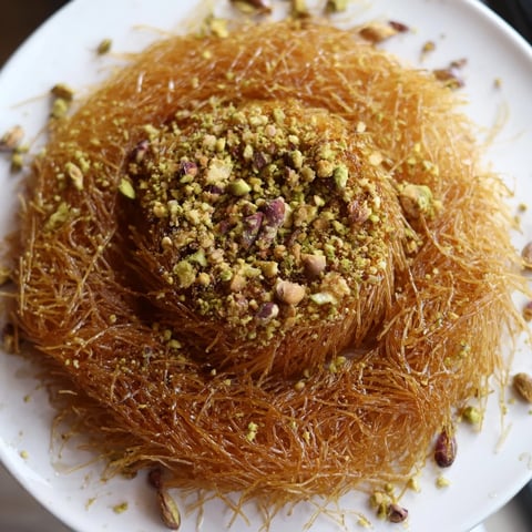 Golden, crispy layers of Egyptian Konafa dessert, glistening under a drizzle of sweet honey syrup.