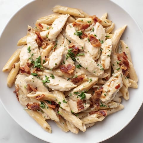 Creamy Chicken Bacon Penne served in a white bowl, with glistening pasta, crispy bacon bits, and tender chicken pieces garnished with fresh parsley.