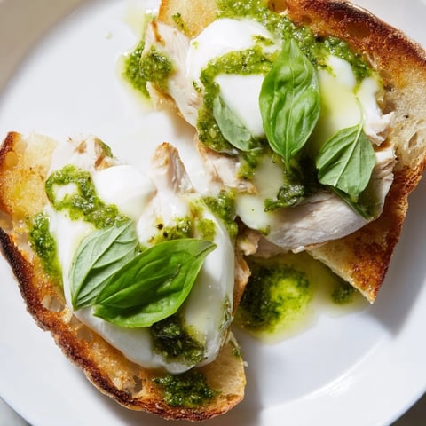 Crisp sourdough toast topped with pesto chicken and creamy burrata, garnished with fresh basil for an Italian-inspired snack.