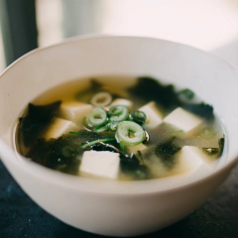 This bowl of steaming Japanese Wakame Soup features tender seaweed and silken tofu in a clear, savory dashi broth, garnished with fresh green scallions.