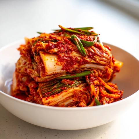 A vibrant bowl of homemade kimchi, featuring crunchy napa cabbage and radish coated in a spicy red gochugaru paste, ready to ferment.  