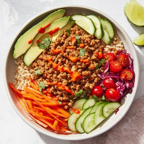 Vibrant plant-based meat bowl featuring colorful veggies and creamy sriracha mayo drizzled.  