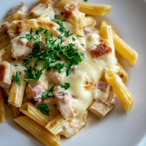 Steam rises from a spoonful of Chicken Alfredo Casserole, revealing tender chicken pieces and gooey cheese over perfectly al dente pasta.