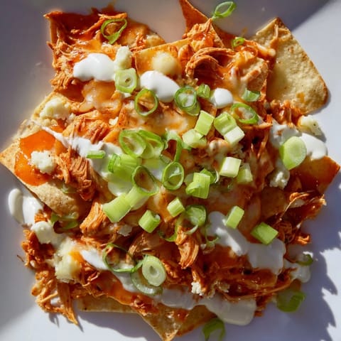 Hot Buffalo Chicken Nachos on a serving platter, garnished with fresh green onions, diced celery, and a drizzle of cool ranch dressing.  