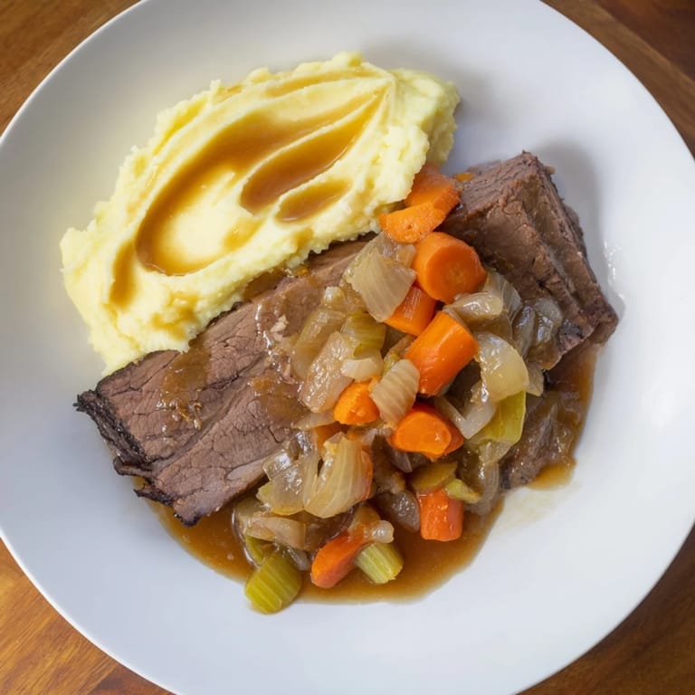 Flavorful classic brisket, a hearty main course, is plated beside a fluffy heap of sweet potato mash.
