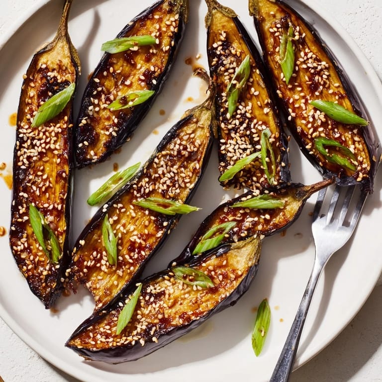Caramelized miso glazed eggplant with crosshatched scoring, garnished with sesame seeds and green onions on a rustic plate.