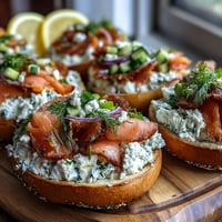 Vibrant spring brunch board with assorted bagels, smoked salmon, fresh vegetables, and creamy herb-infused cream cheese for sharing.